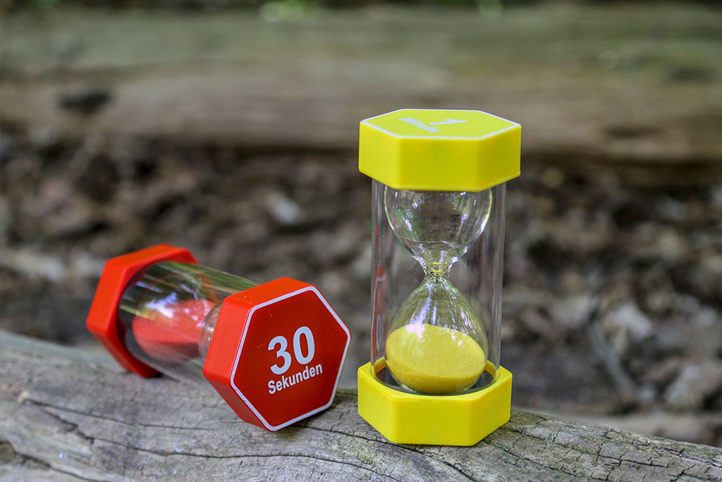 Zwei Sanduhr-Timer, einer rot mit der Aufschrift „30 Sekunden“, stehen auf einem Baumstamm